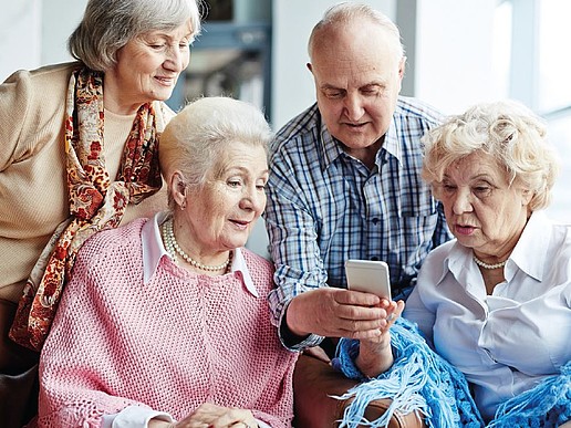 Four senior citizens sit together and look at a cell phone display