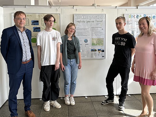 The dean, two students, one student and the vice-rector stand in front of white back walls with posters on the topic of sustainability pinned to them and smile into the camera.