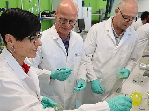 In the laboratory, a biology teacher holds a pipette in her hand. Her colleagues are watching the experiment.