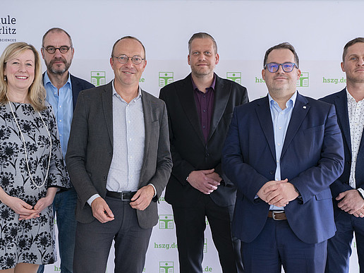 The university management, the Energy Minister and the project partners stand in front of the HSCG press wall and smile into the camera.