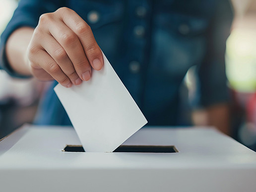 A man puts a white piece of paper into a white ballot box.