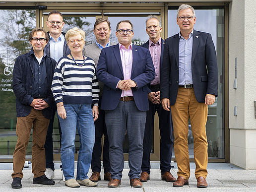 The university rector and the rectors stand on the stairs in front of building one for the group photo and smile into the camera.