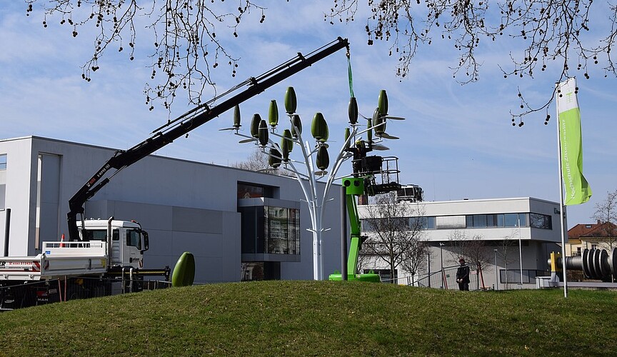 Montage vom Wind- und Photovoltaikbaum: Ein LKW mit Kran hebt einen Windgenerator an das errichtete Grundgestell vom Baum