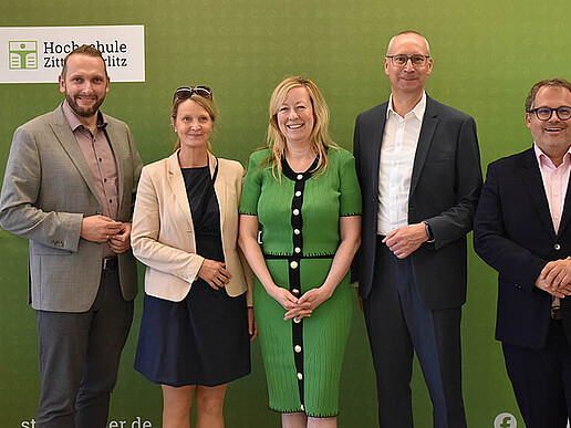 Eine Delegation der HSZG und der Stadt Bautzen steht vor der grünen Pressewand und lächelt in die Kamera.