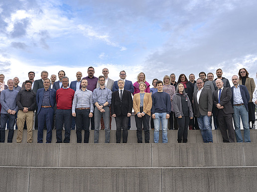 On a roof terrace, the members of the Extended Senate stand in several rows on stone steps.